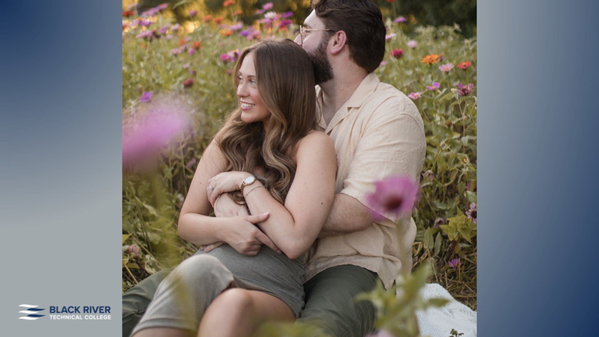 A couple sits together in a colorful wildflower field, with the man embracing the woman from behind as she smiles, with Black River Technical College branding.